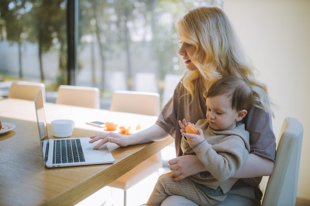 working mom on the laptop while holding her baby at home